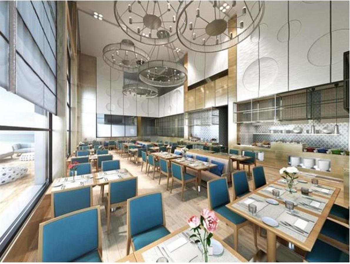 Grand Swiss-Belhotel Waterfront Seef Sanabis Esterno foto The photo depicts a modern restaurant interior featuring a spacious and bright dining area. The decor includes wooden flooring and light wooden furniture, with tables set neatly with blue chairs. Each table has a white tablecloth, plates, cutlery, an