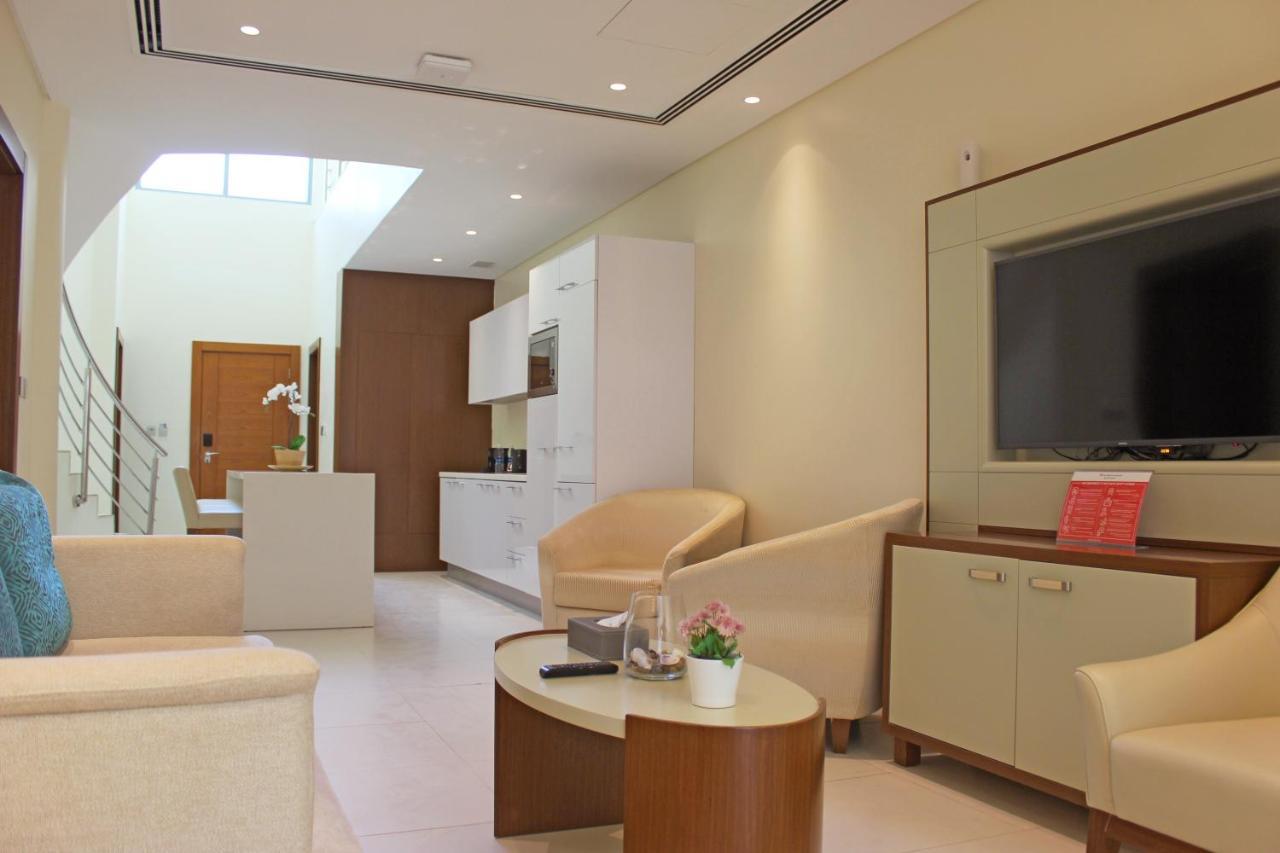 Grand Swiss-Belhotel Waterfront Seef Sanabis Esterno foto The photo displays a modern and stylish interior space, likely a living room or lounge area. The design features light-colored walls and furnishings, creating a bright and airy atmosphere. 

In the room, there are two armchairs and a small round coff