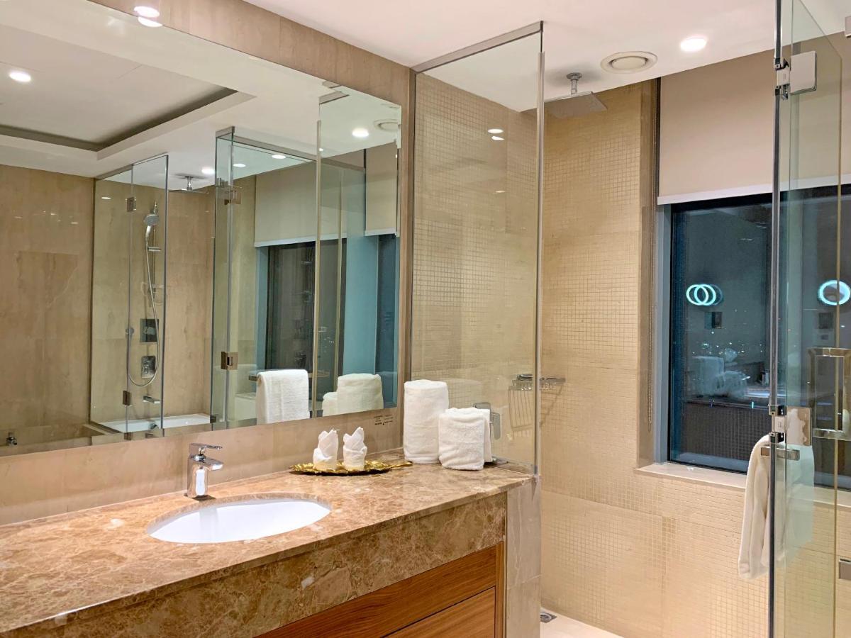 Grand Swiss-Belhotel Waterfront Seef Sanabis Esterno foto The photo shows a modern bathroom designed with a sleek and elegant aesthetic. It features a large vanity with a round sink and a countertop made of marble or a similar stone. The walls and floors appear to be tiled with a light-colored stone, giving