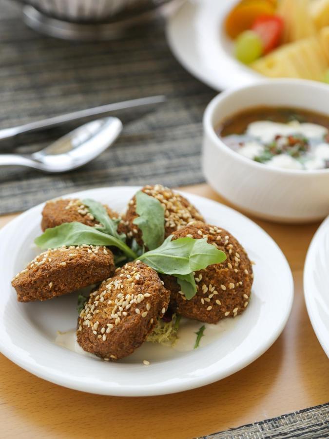 Grand Swiss-Belhotel Waterfront Seef Sanabis Esterno foto The photo shows a plate of golden-brown, fried falafel balls, which are often made from ground chickpeas or fava beans and seasoned with various spices. They are garnished with fresh greens, possibly arugula or similar leafy herbs, and sprinkled with