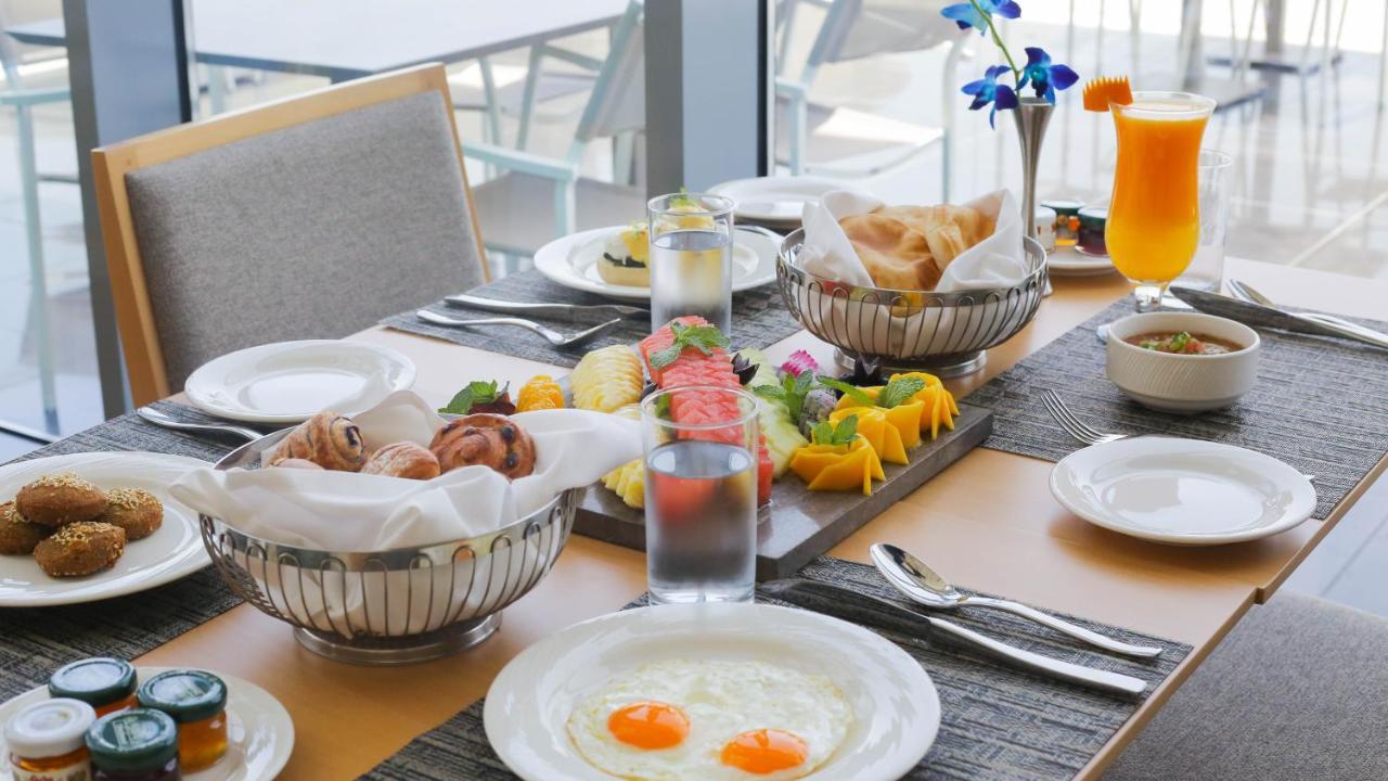 Grand Swiss-Belhotel Waterfront Seef Sanabis Esterno foto The photo displays a beautifully arranged breakfast table. At the center, there's an assortment of fresh fruits, including watermelon and mango, presented on a wooden platter. Around the table, there are dishes containing pastries and bread, neatly p